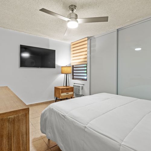 This modern bedroom is designed for relaxation, featuring a large bed with plush pillows and a convenient, sleek media setup for entertainment.