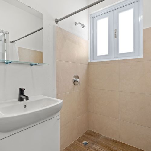 Where cleanliness and simplicity meet, featuring a spacious sink area and a refreshing shower.