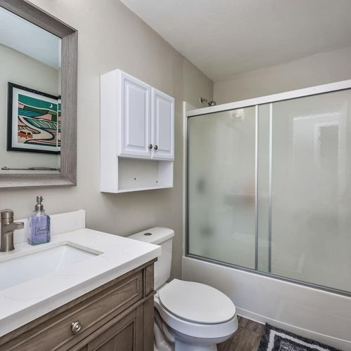 - clean and simple bathroom featuring a full size vanity and framed mirror
- frosted glass shower doors offer privacy and a polished modern feel
- over toilet storage cabinet adds extra space for essentials and toiletries