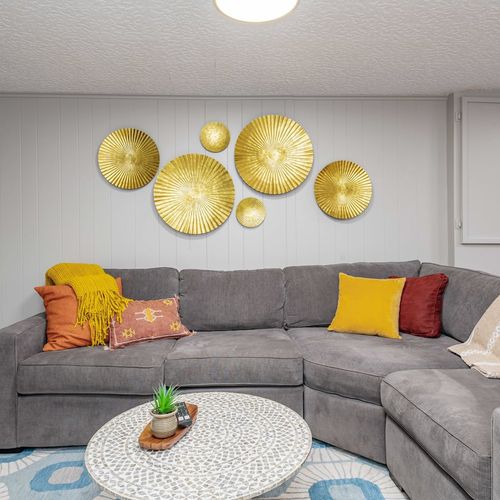 - inviting lounge, ideal for game nights or movie marathons
- golden wall art and cheerful pillows add a playful, modern vibe to the cozy basement retreat
- mosaic coffee table and plush throws make this a perfect spot to relax after a day of adventu
