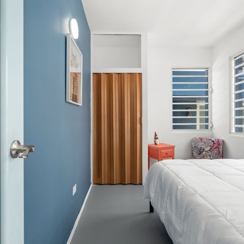 This spacious room features modern amenities and sleek design. The blue accent wall adds a pop of color to the space. A piece of modern artwork hangs on the blue wall adding an artistic touch to the room. A large window allows ample natural light to flood into space, enhancing its brightness.