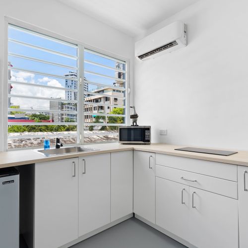 The modern white cabinets are enhanced by sleek stainless steel appliances, illuminated by a large window, which brings brightness and contemporary style to the kitchen area.
