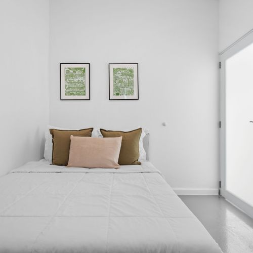 Relájese en esta elegante habitación con una cama bien hecha, paredes blancas y un toque de verde en obras de arte enmarcadas.