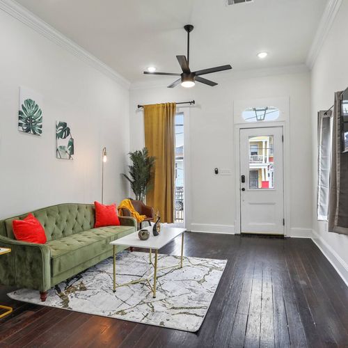 Welcoming living room w/ a green sofa, ceiling fan & warm wood floors.