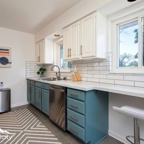 - chic galley kitchen with two tone cabinetry, subway tile backsplash, and sleek counters
- stainless appliances and bar seating make cooking and socializing easy
- large windows bring in sunlight and frame views of the backyard greenery