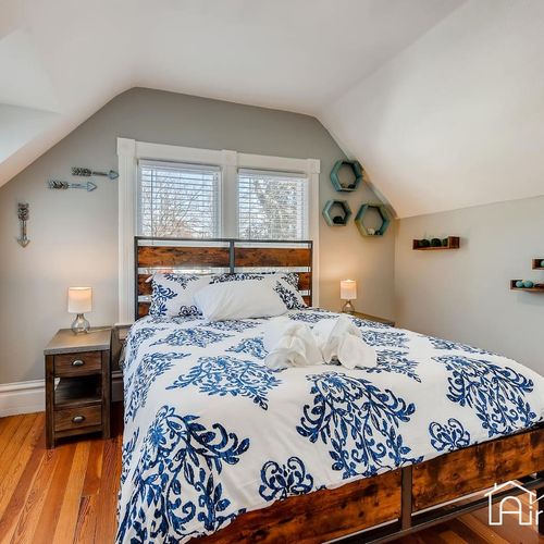 - attic style bedroom features a full bed with botanical linens and a rustic wood frame
- two windows and dual nightstands with soft glow lamps add comfort and ease
- wall mounted accents and honeycomb shelves bring playful style