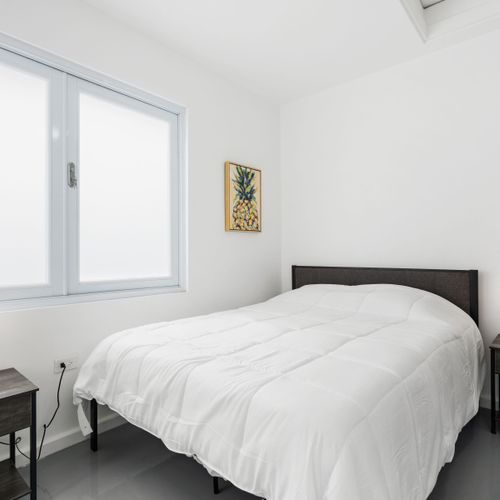 Un dormitorio sereno que cuenta con una lujosa cama tamaño queen adornada con sábanas blancas impecables, flanqueada por mesas de noche contemporáneas e iluminación ambiental, que ofrece un refugio tranquilo.
