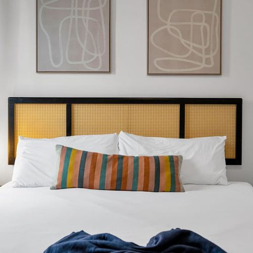 Bedroom w/ a woven headboard & striped pillows — relaxed & inviting.