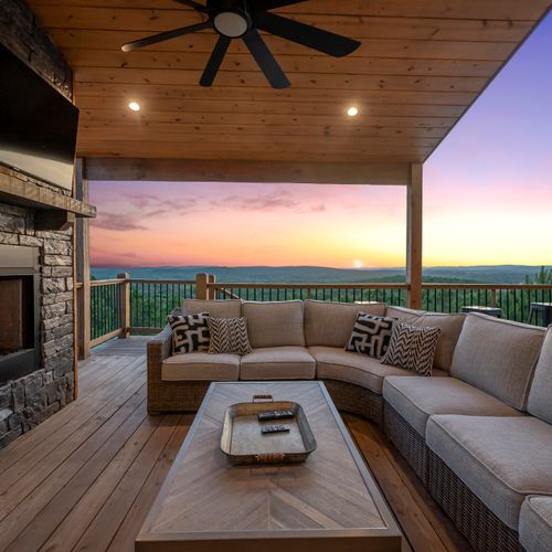 The covered patio has an oversized sectional around a stone gas fireplace.