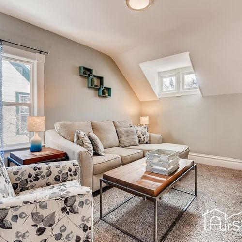 - relaxing upstairs living room with plush sectional, floral chair, and sloped ceiling charm
- windows on both sides fill the room with soft, natural light all day
- great for quiet reading, conversation, or cozy evening relaxation