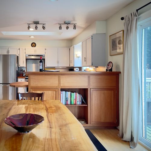 Gather around the handcrafted dining table for shared meals or morning coffee, with the kitchen just steps away and deck access nearby. Warm wood details, natural light, and easy indoor-outdoor flow.