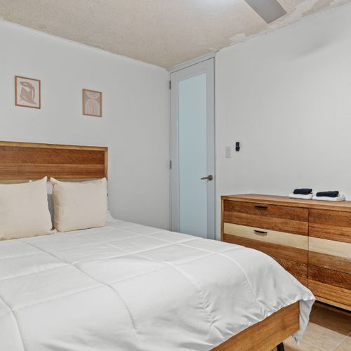 Cozy up in this serene bedroom featuring a sleek wooden bed frame and soft, neutral tones for a restful night's sleep.