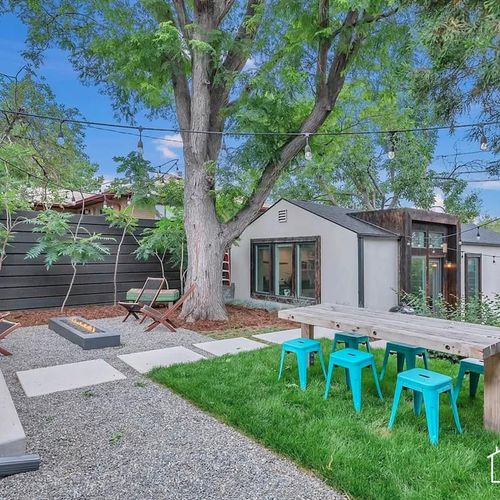 - charming backyard oasis featuring a cozy fire pit & string lights for evening ambiance
- dine al fresco at the rustic wood table with vibrant turquoise stools under the trees
- surrounded by greenery & privacy fencing for a peaceful, relaxed outdoo