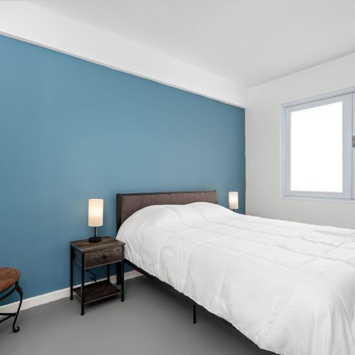 Enjoy a restful night in this modern bedroom featuring a comfortable bed, accentuated by the calming blue wall and ample natural light from the large window.