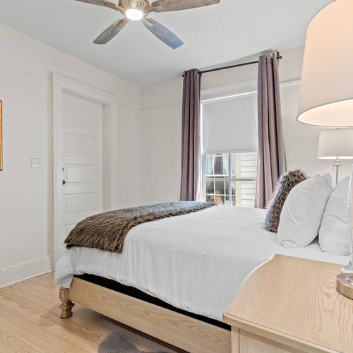 Bright primary bedroom w/ crisp white bedding & warm overhead lighting.