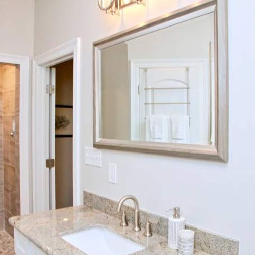 Bright bathroom w/ a framed mirror & warm wood-toned vanity.