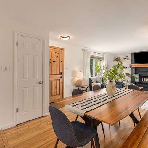 - view from the dining area shows the handcrafted wood table, front entry, and living room
- bright, stylish, and welcoming with a centerpiece vase and gallery decor
- great for shared meals, group planning, or casual conversation