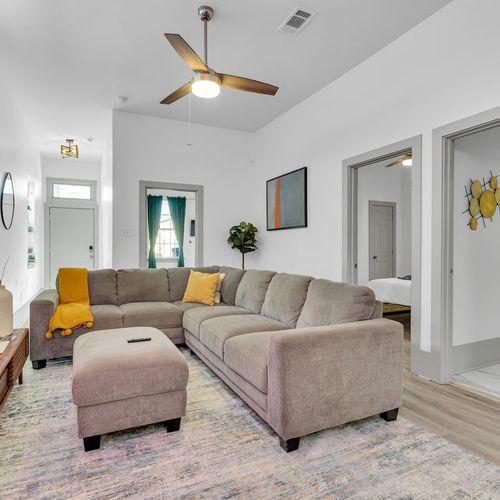 Bright living room w/ plush sofa, warm tones, & ceiling fan to kick back after a long day.