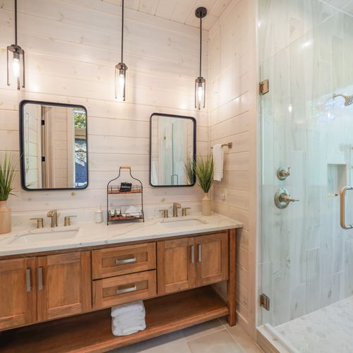 This bath comes with a spacious double-sink vanity with warm wood tones, crisp white countertops, and whitewashed wood walls—elegance and functionality meet in perfect harmony.