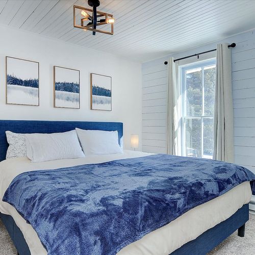 - spacious king bedroom with sleek blue upholstered frame and crisp white linens
- large picture window fills the room with light and stunning mountain scenery
- minimalist décor with nature themed artwork adds a tranquil, sophisticated vibe