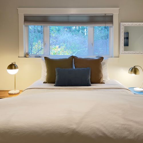 A peaceful, light-filled bedroom with a comfortable bed, soft linens, and reading lamps on both sides. Wake up to leafy views through the window and enjoy a quiet, cozy space designed for restful nights and relaxed mornings.