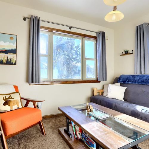 - bright and inviting space with large windows that frame peaceful pine views
- cozy up on the plush futon or the orange accent chair with a moose pillow touch
- coffee table stocked with games and books adds a playful, homey vibe