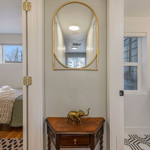 - elegant hallway accent with a golden mirror and charming brass elephant welcoming you in
- peek into a cozy bedroom with fresh linens and soft natural light
- stylish black vanity and patterned tile bring character to the adjoining bathroom