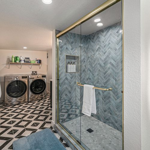 - multi functional space combines a luxe glass shower with a laundry setup
- chevron tile shower wall, brass accents, & patterned floors elevate your daily routine
- easily freshen up & do laundry without stepping out of this beautifully styled area