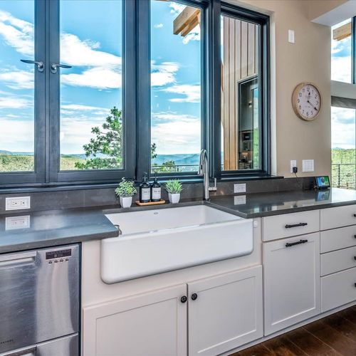- wash up with a view at this large farmhouse sink framed by oversized black windows
- modern matte countertops and curated greenery create a calm clean atmosphere
- enjoy peaceful mountain scenery with every rinse, slice, or pour