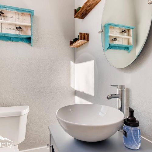 - modern half bath with a white bowl sink, wall mounted faucet, and oval mirror
- rustic floating shelves and teal vintage boxes add unique decorative storage
- natural light and neutral walls create a clean welcoming vibe