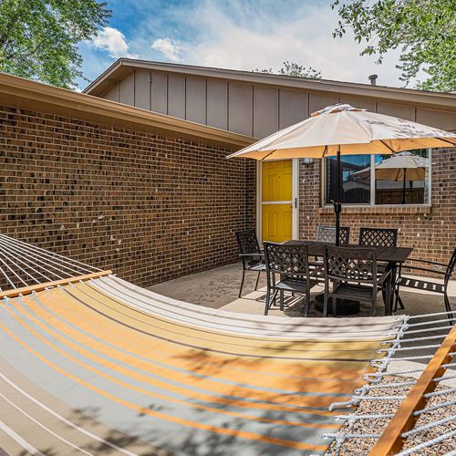 - brick patio offers hammock relaxation and shaded dining under a large umbrella
- dine alfresco with seating for six just steps from the bright yellow door
- surrounded by trees and blue skies this is your backyard escape zone