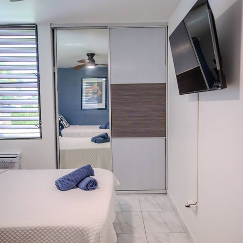 This well-appointed room offers comfort and convenience with a mounted flat-screen TV for entertainment, ample storage in the sliding mirror closet, and a ceiling fan for comfort. Perfect for a relaxing stay.