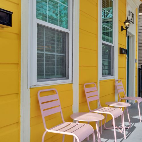Sunny yellow exterior w/ a private patio & pink chairs — a cheerful spot to sip & unwind.