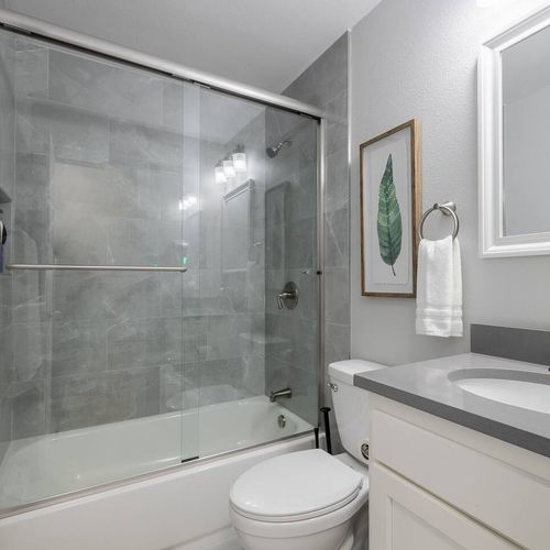 - refresh in a sleek tub and shower combo with elegant gray tiling and glass doors
- soft lighting and a wide mirror offer comfort and clarity for your daily routine
- thoughtful decor like the leaf print and neutral palette bring a spa like calm