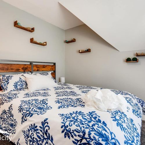 - charming bedroom with bold blue bedding and creative wooden floating shelves
- sloped ceiling and corner layout make this room cozy and unique
- wood accent headboard and neutral tones give the space rustic modern balance