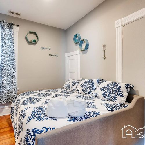 - comfy full size bed is dressed in floral linens with neatly folded towels ready for guests
- decorative arrows and shelves add artistic flair to this restful bedroom retreat
- hardwood floors and soft lighting make this space both fresh and cozy