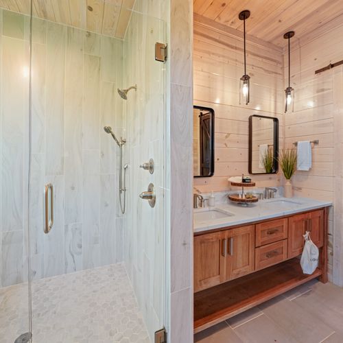 Step into luxury with a spacious walk-in shower featuring sleek glass doors and stunning tilework, complemented by warm wood tones and crisp white countertops.