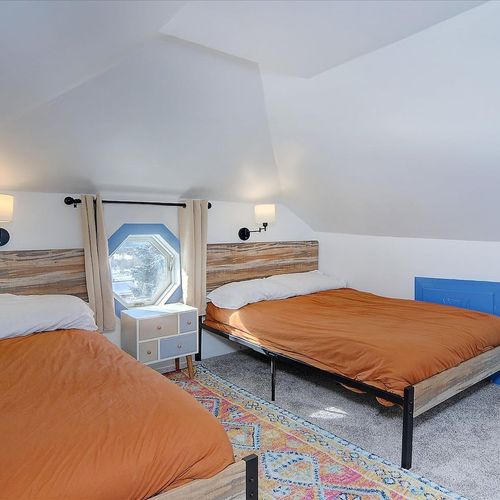 - twin beds with matching reclaimed wood headboards ideal for families or friends
- vaulted ceiling adds character while wall sconces provide ambient glow
- center nightstand and window nook make this space both functional and charming
