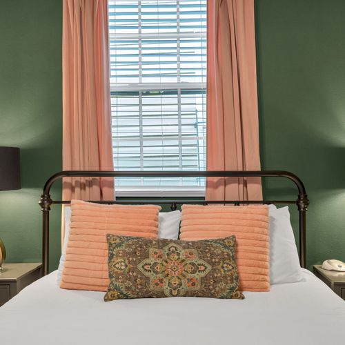 Cozy bed w/ soft peach & patterned bedding bathed in natural light.
