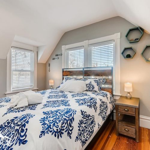 - sun filled bedroom with rustic wood headboard, double nightstands, and triple windows
- crisp blue and white bedding and warm hardwood floors create a calm retreat
- modern wall decor and soft lighting offer a soothing place to unwind