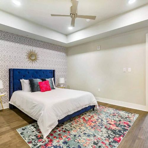 Bright bedroom w/ blue upholstered bed, bold floral bedding & ensuite access.