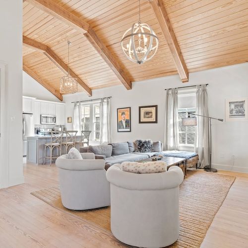 Sunlit living room w/ soaring wood-beam ceilings, a chandelier & plush seating for the whole group