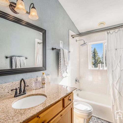 - fresh and bright bathroom with granite countertop and classic vanity lighting
- enjoy a soothing soak in the tub while gazing out at serene forest views
- crisp white tile and natural light create a clean and spa like retreat