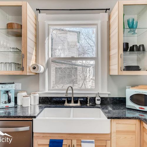 - farmhouse sink beneath a bright window pairs beautifully with wood cabinetry and granite counters
- glass front cabinets and open shelves display stylish dishware and mugs
- includes microwave, coffee maker, toaster, and essential kitchen tools