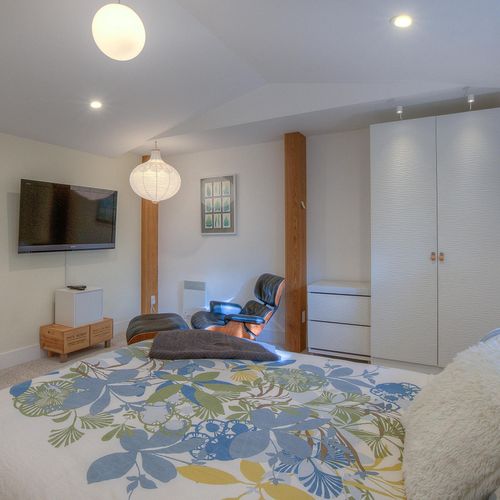 Guest bedroom has a TV and Emmes chair for relaxing.