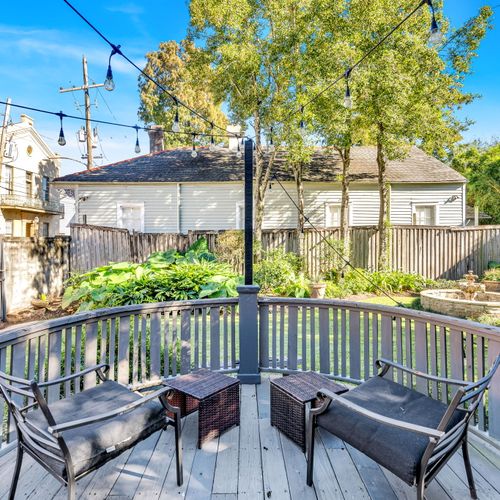 Cozy outdoor seating area overlooking a lush garden with a serene fountain, surrounded by string lights for evening charm.