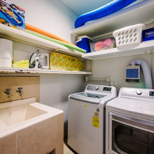 In-unit laundry room with LG washer and dryer, utility sink, and shelves stocked with pool floats and beach gear.