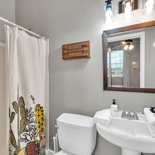 Bright bathroom w/ a tub, wood-framed mirror & bold floral curtain for a homey touch.
