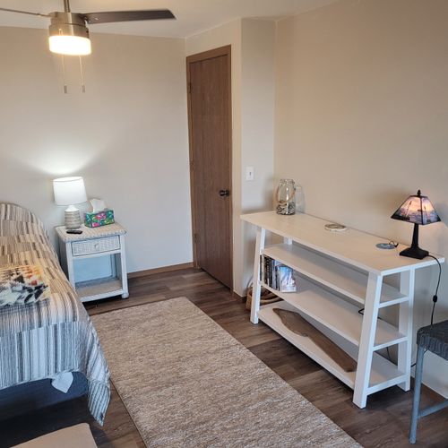 BEDROOM #1 (PRIMARY):  Features a queen-size bed, sofa bed, lakeview, private ensuite bathroom, private entrance from the back patio, private television, nightstand, lamp, ceiling fan, dresser, and shelves