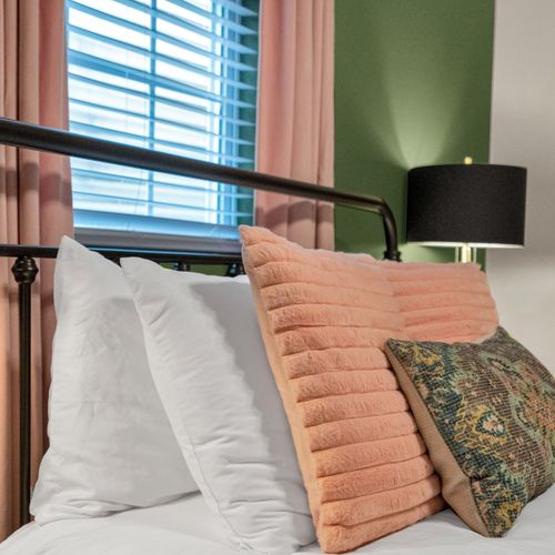 Bedroom w/ green walls, blush curtains & a bold patterned rug underfoot.